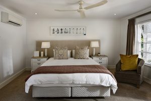 Tipos de hospedagem - uma cama branca numa quarto branco de hotel, piso marrom, poltrona marrom ao lado da cama com uma almofada.