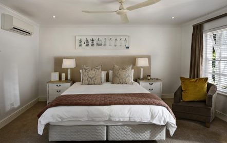 Tipos de hospedagem - uma cama branca numa quarto branco de hotel, piso marrom, poltrona marrom ao lado da cama com uma almofada.